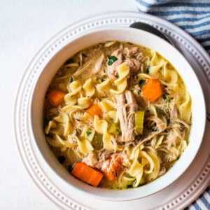 A bowl of Chicken Noodle Soup with carrots and celery on a table.