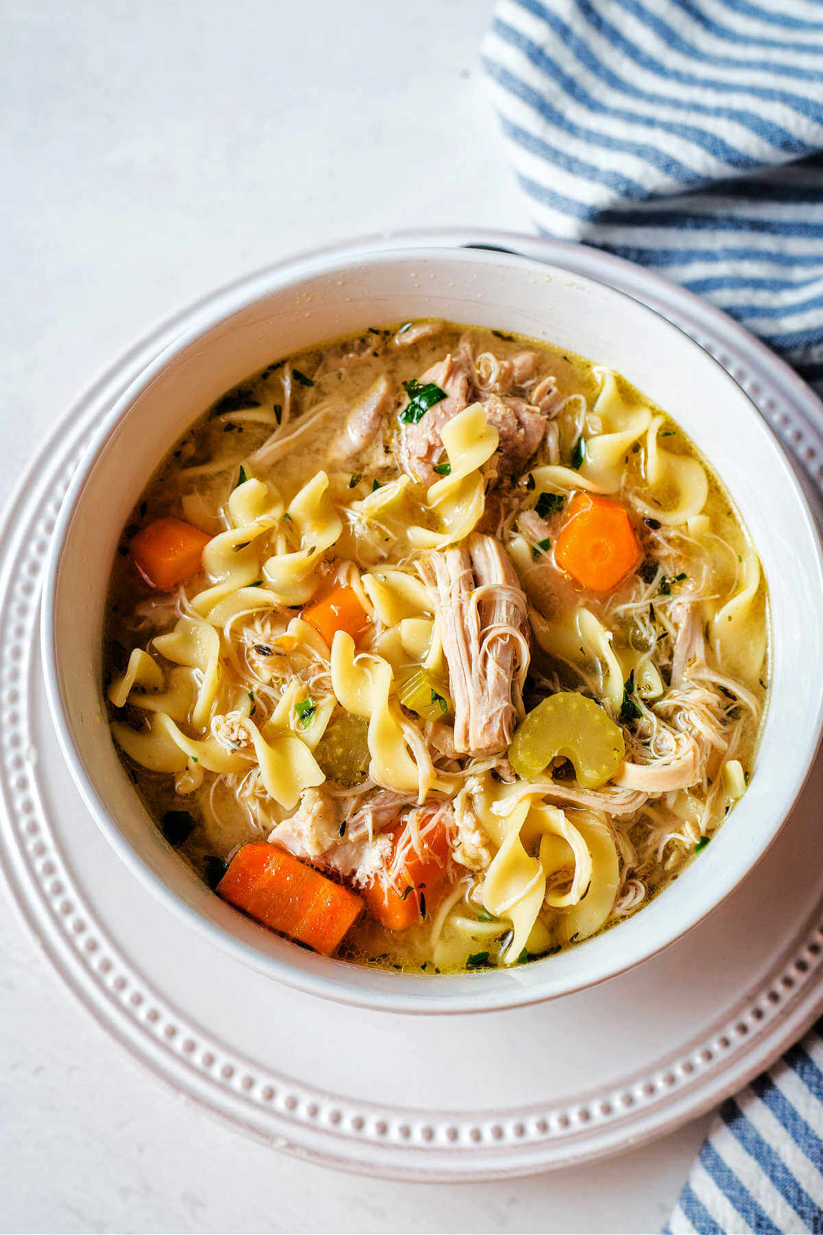 Instant pot chicken noodle soup served in a bowl on a white plate.