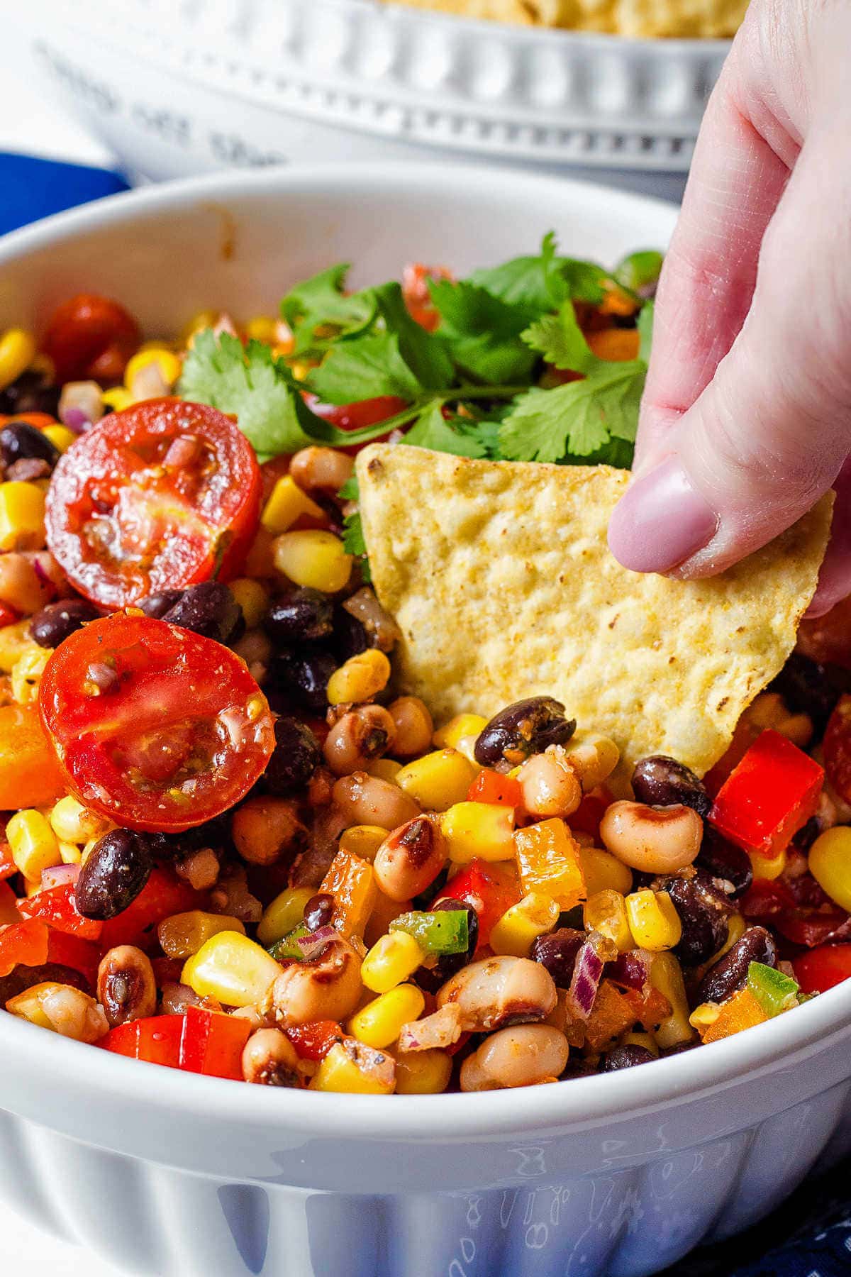 Hand dipping a tortilla chip into a bowl of cowboy caviar.