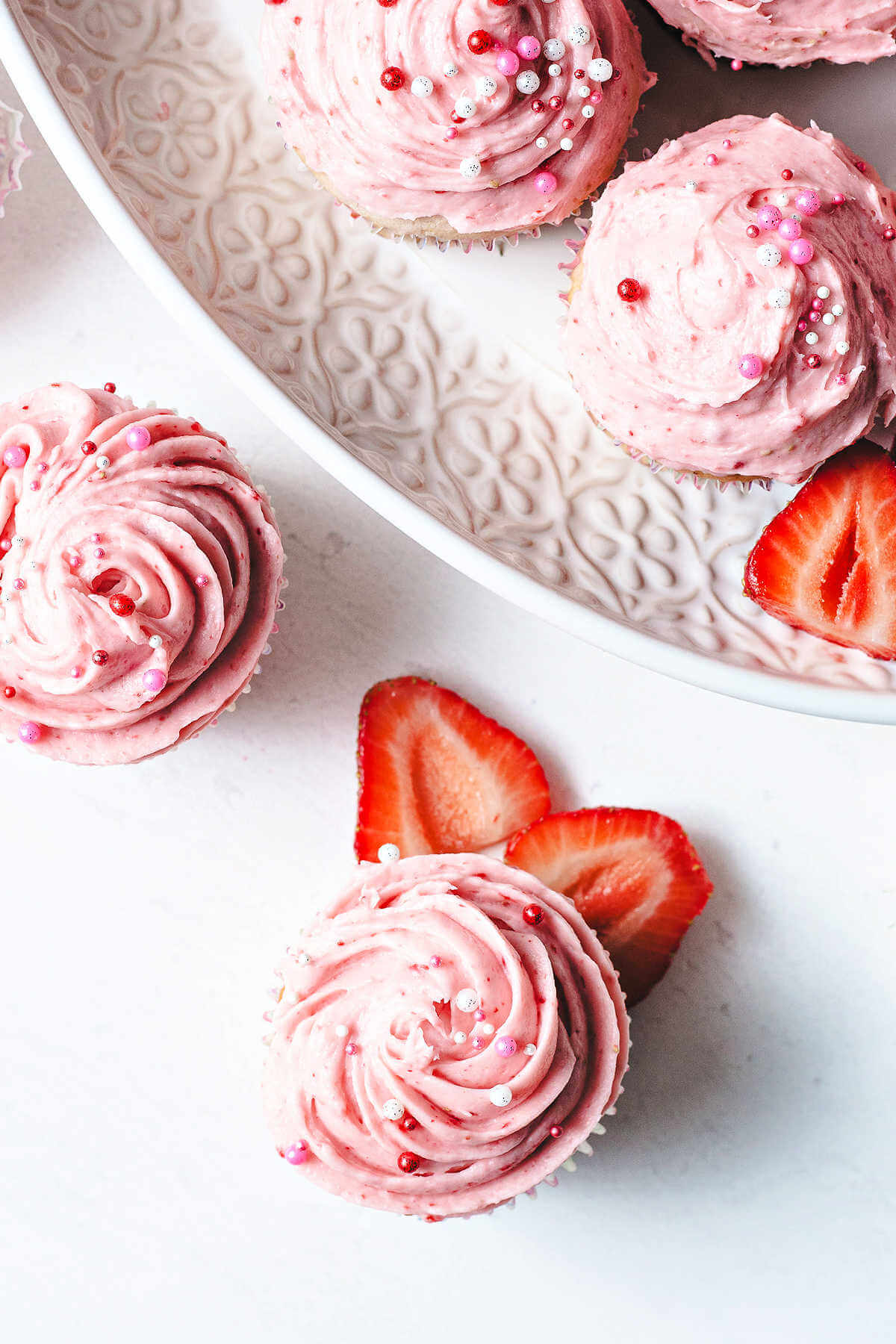 Overhead shot of strawberry cupcakes with frosting and sprinkles.