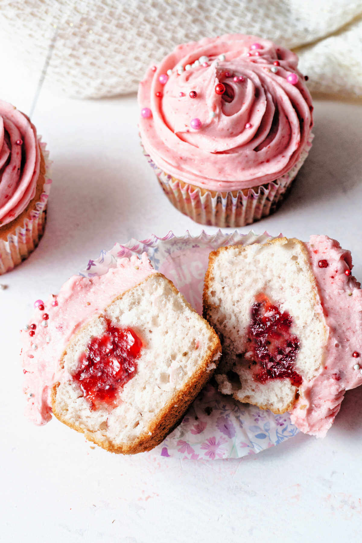 One strawberry cupcake cut in half to show the inside next to a whole cupcake.