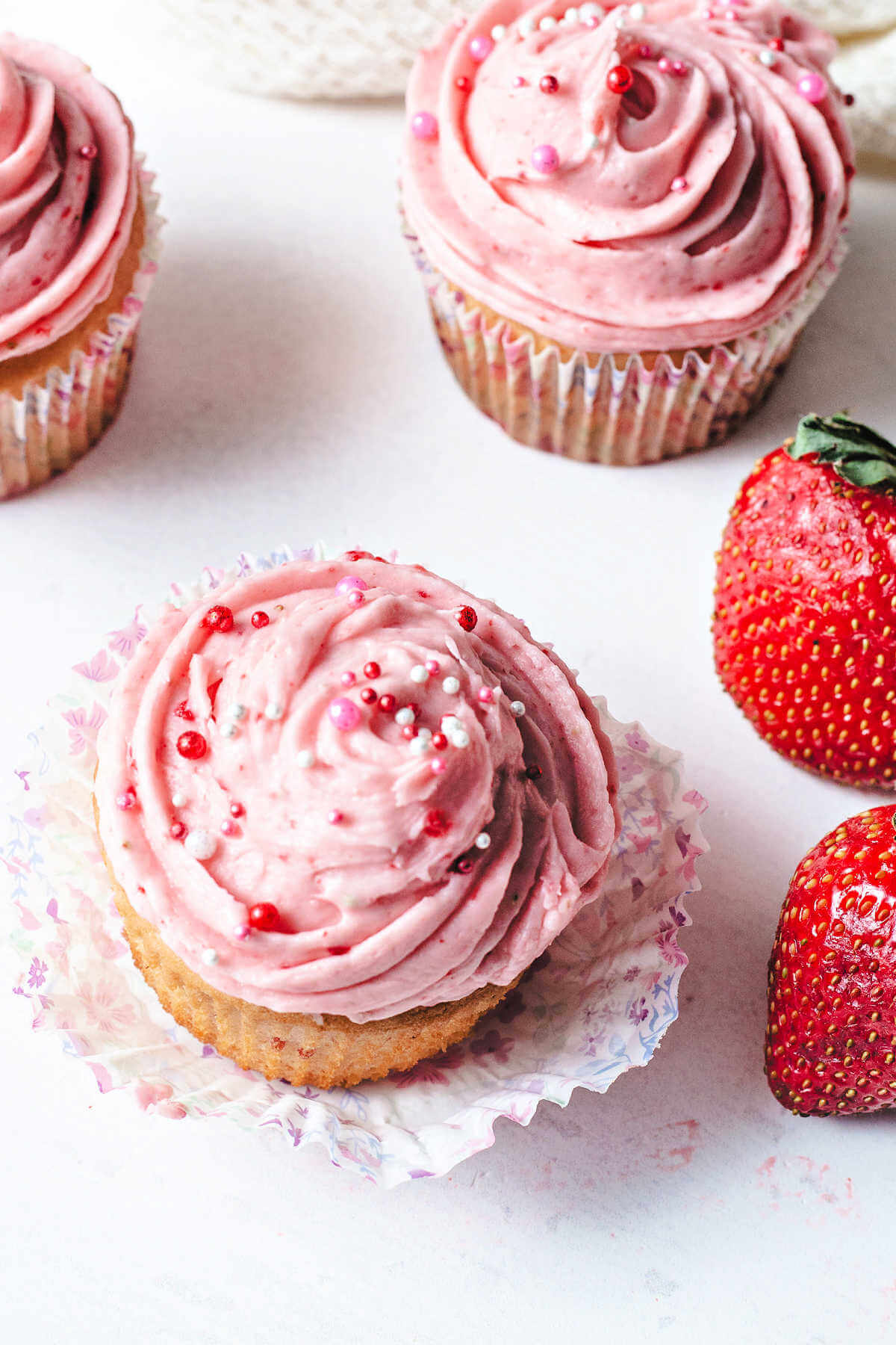 Strawberry cupcake on a wrapper next to fresh strawberries.