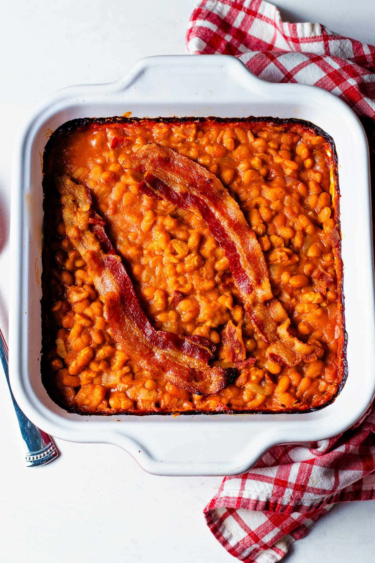 Overhead shot of finished baked beans with bacon in a white baking dish.