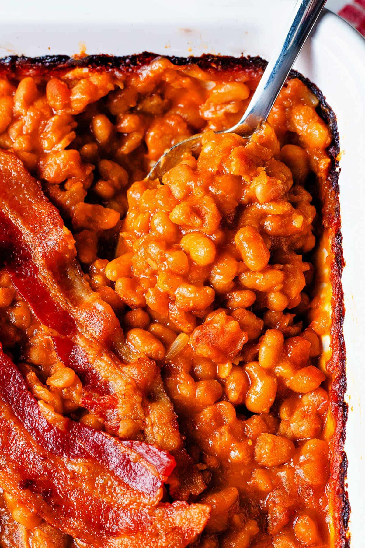 Spoon scooping up a portion of baked beans with bacon.