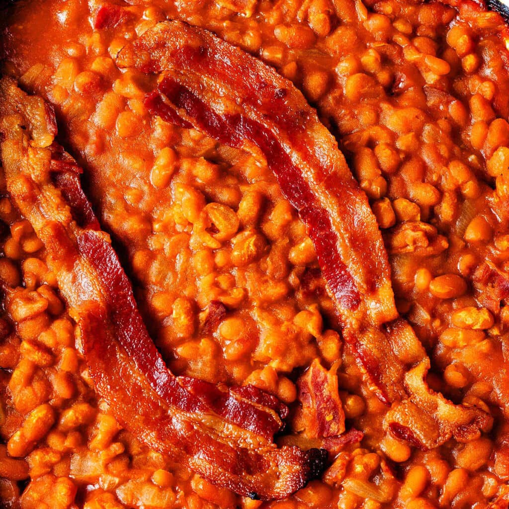 Two pieces of bacon on top of easy baked beans in a baking dish.