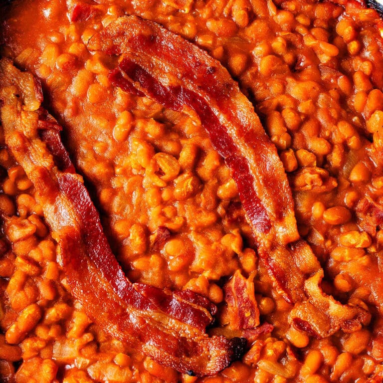 Two pieces of bacon on top of easy baked beans in a baking dish.