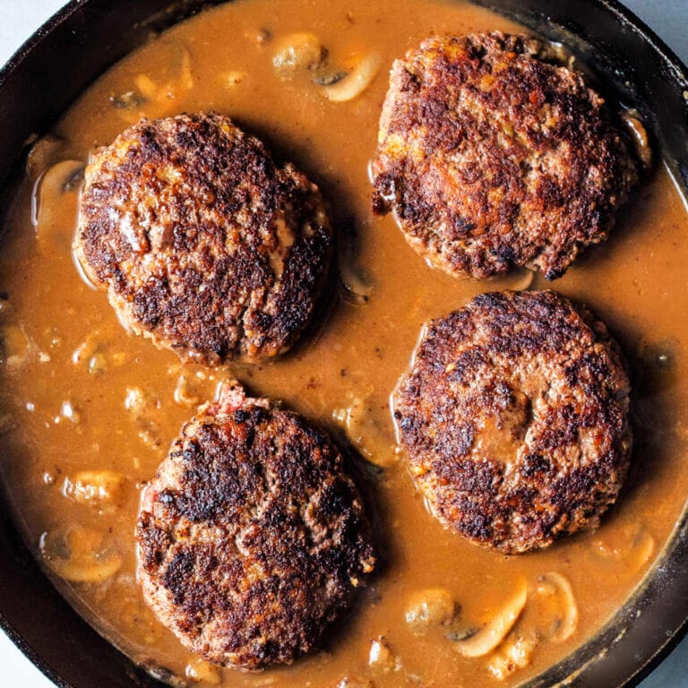 Hamburger steaks nestled in mushroom gravy in a cast iron skillet.