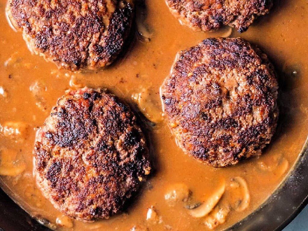 Hamburger steaks added back to the skillet of mushroom gravy.