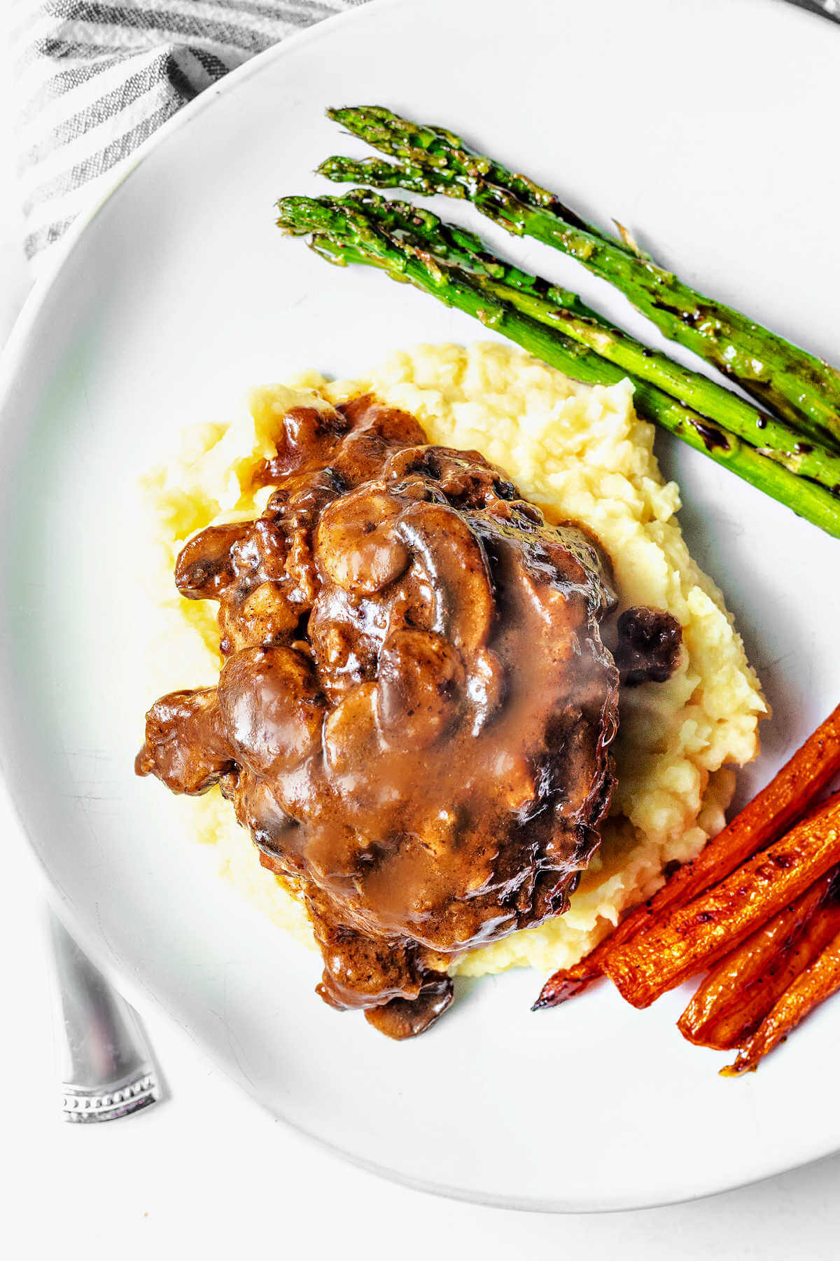 Hamburger steak served on a plate with mashed potatoes and mushroom gravy on top.