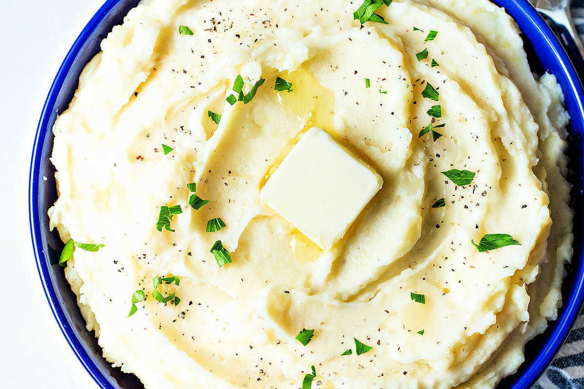 Pat of butter placed on top of finished mashed potatoes in a bowl.