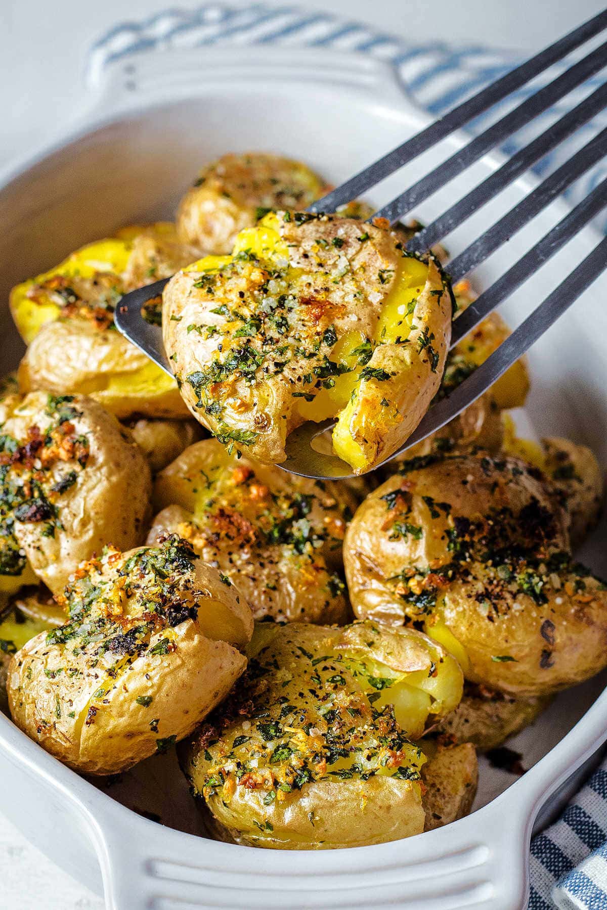 Spatula picking up a garlic smashed potato from a bowl of them.