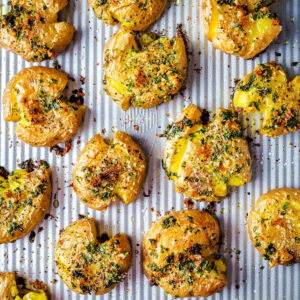 Smashed potatoes with garlic and lemon lined up on a sheet pan.