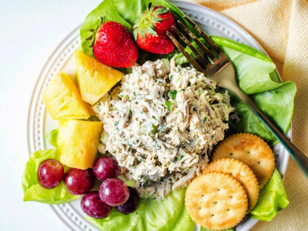 A scoop of Classic Chicken Salad on a plate with fresh fruit and crackers,
