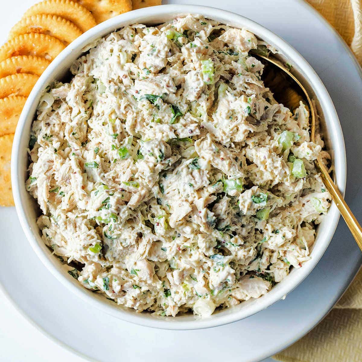 A bowl of classic chicken salad on a plate with crackers.