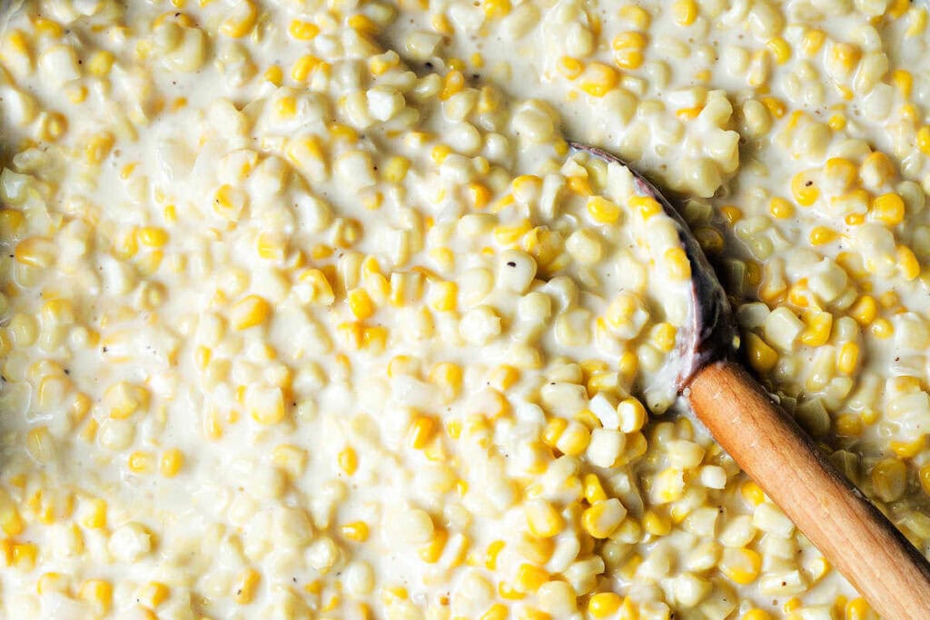 Close up of creamed corn with a wooden spoon.
