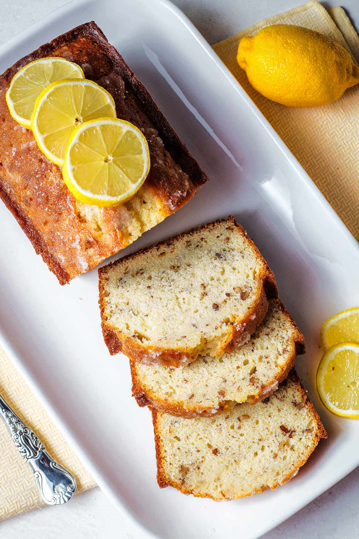 A sliced loaf of lemon bread on a platter with lemon slices on top.