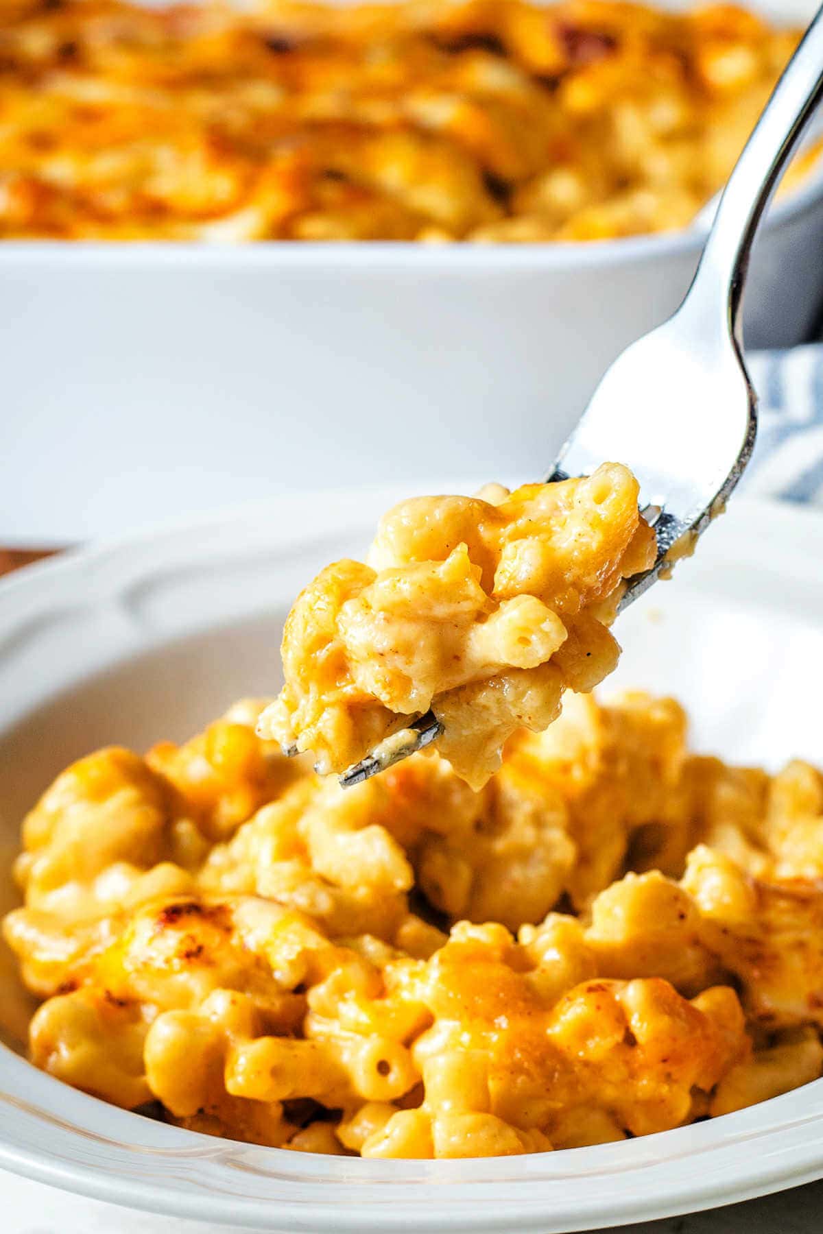 Fork with a bite of macaroni and cheese on it with a bowl of it below.