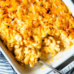 Macaroni and Cheese in a baking dish with a serving spoon scooping out a serving.
