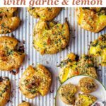 Smashed potatoes seasoned with garlic and lemon on a baking sheet.