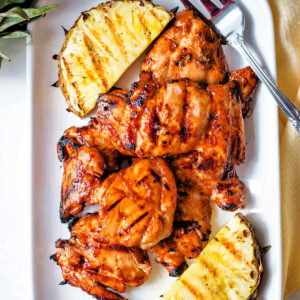 Huli huli chicken on a serving platter next to grilled pineapple.