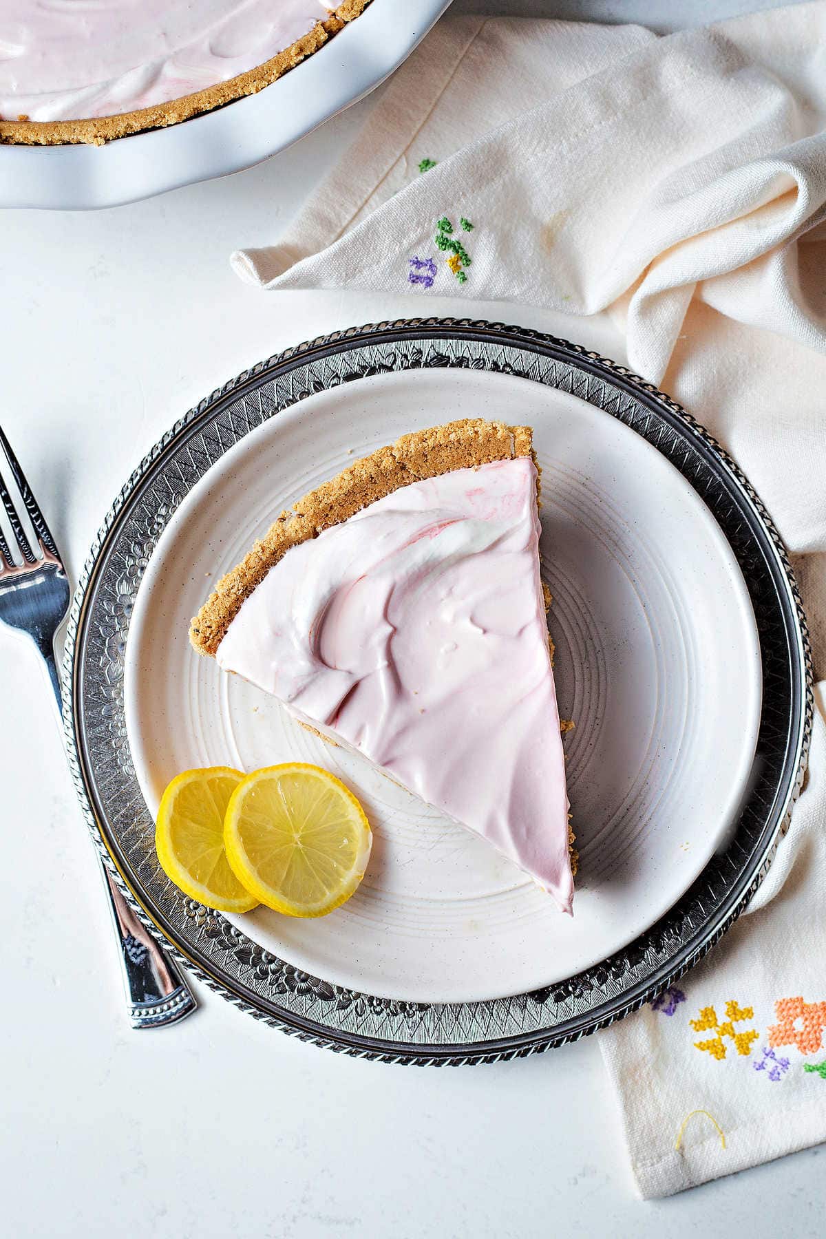 Overhead shot of a slice of pink lemonade pie next to two slices of lemon.