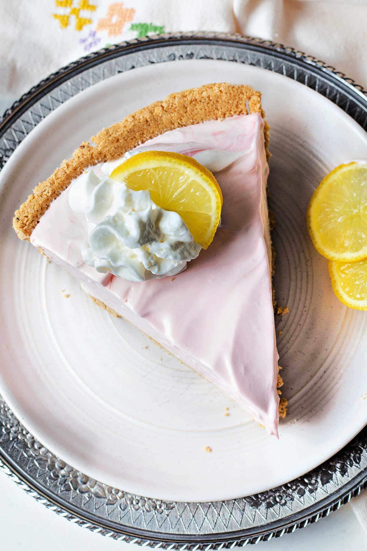 Slice of pink lemonade pie on a plate, garnished with whipped cream and a slice of lemon.