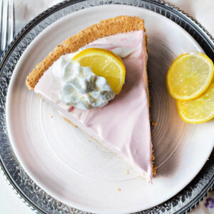 A slice of lemonade pie on a plate garnished with whipped cream and a lemon slice.