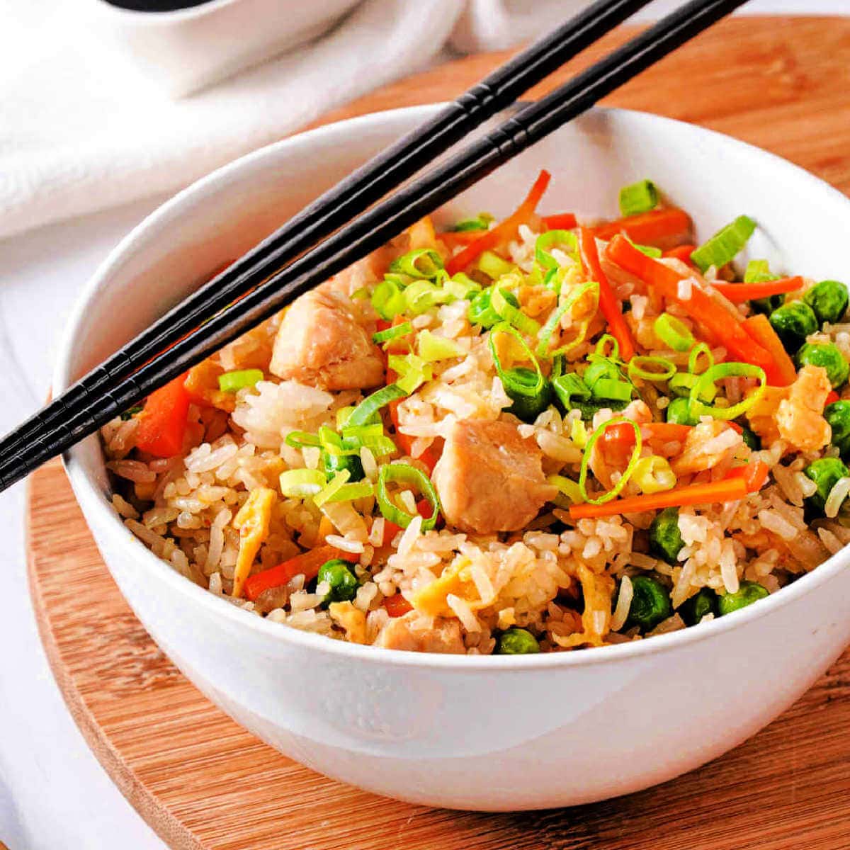 Side view of a bowl of chicken fried rice with chopsticks.
