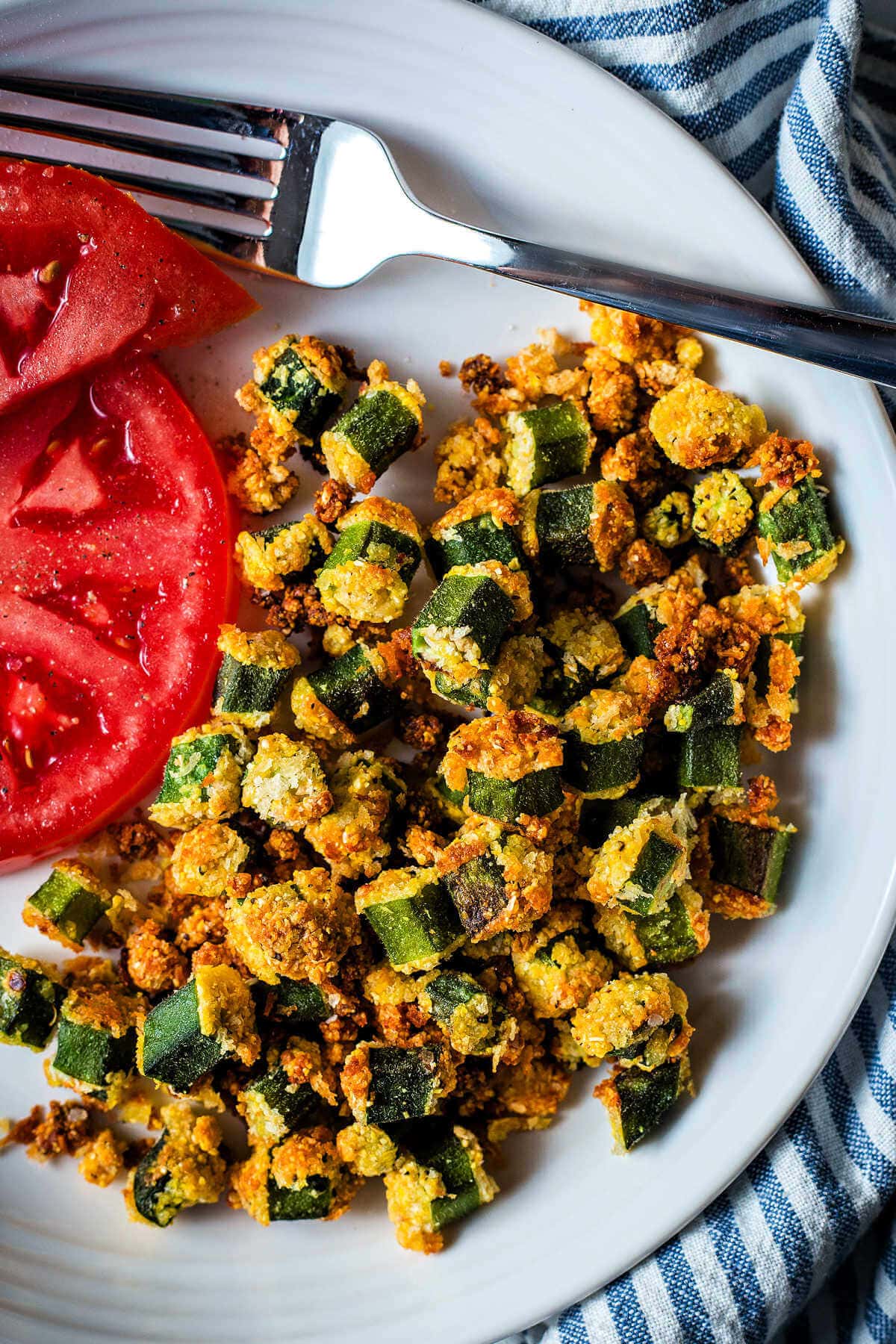 Crispy okra on a plate with sliced tomatoes.