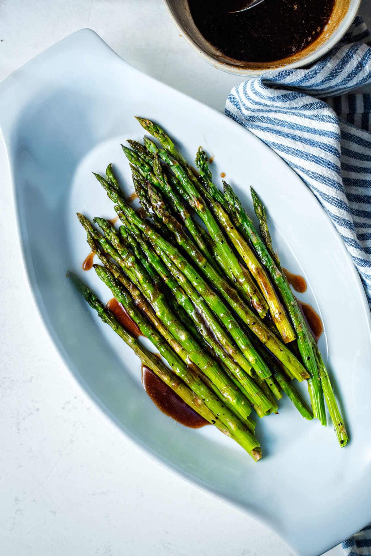 Roasted asparagus in a serving dish with brown butter mixture drizzled over the top.