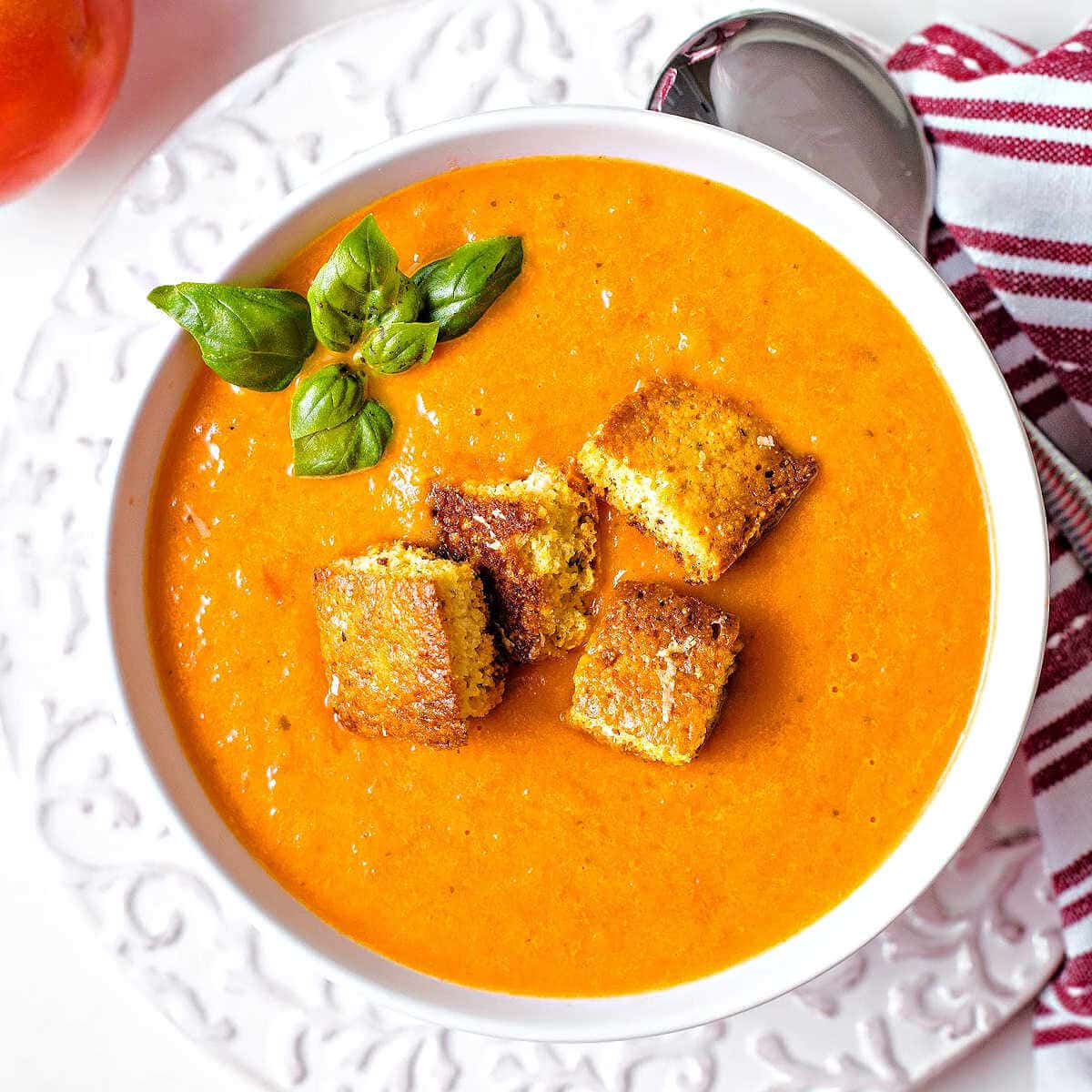 A bowl of tomato soup with cornbread croutons on a table.