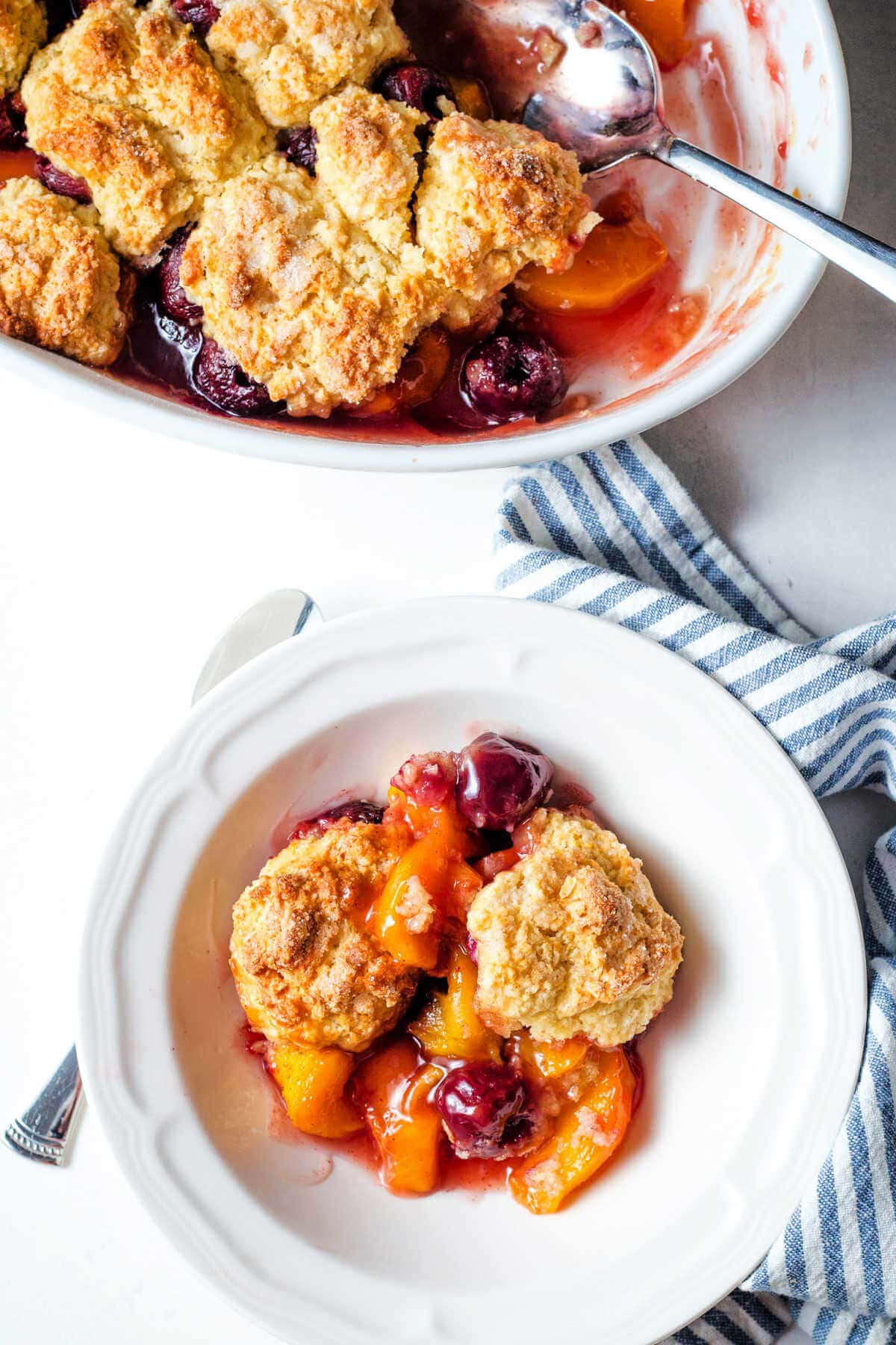 Peach cherry cobbler in a bowl next to the baking dish of cobbler.
